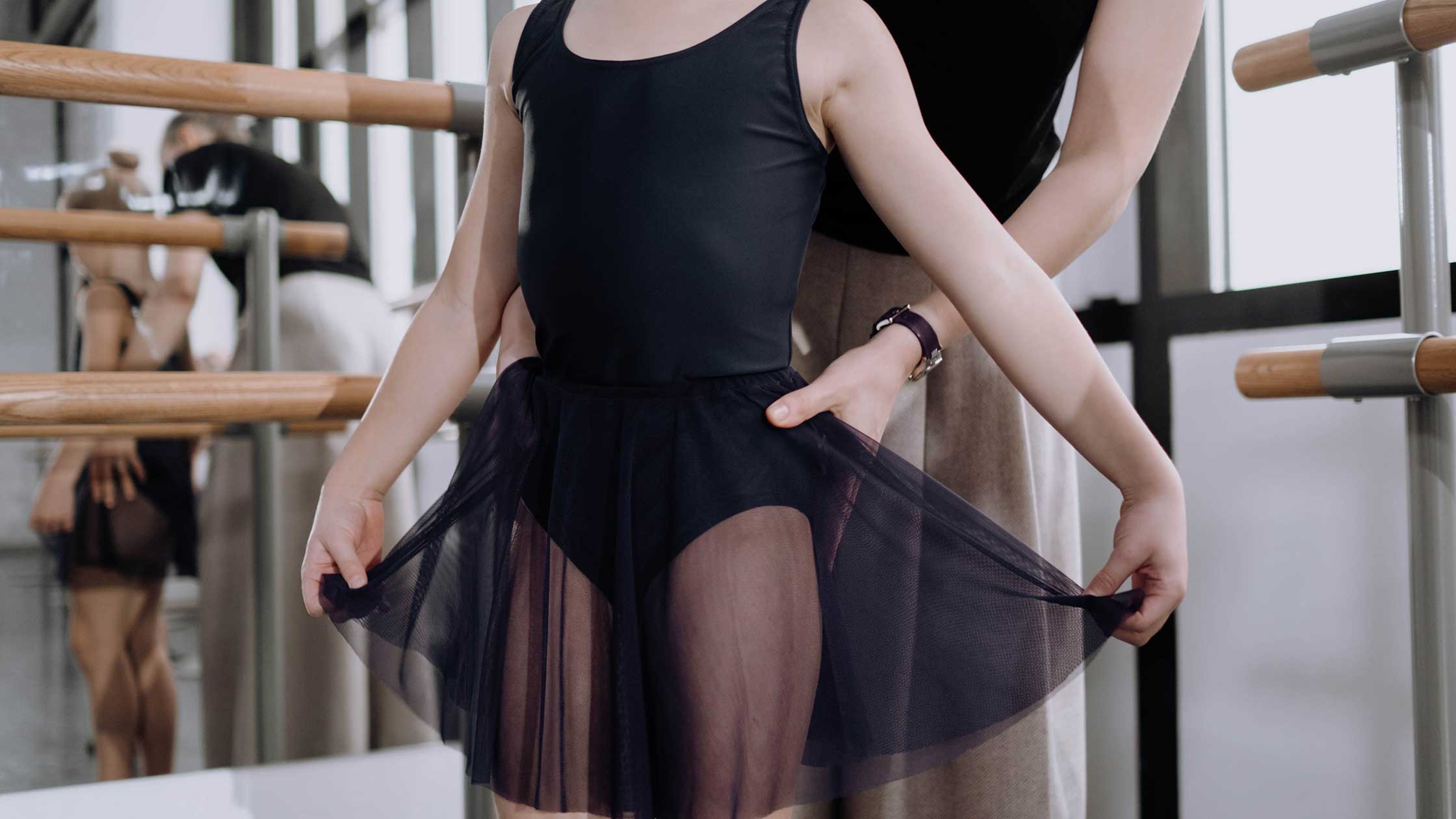 Jeune danseuse portant un justaucorps noir et une jupe de ballet en tulle pendant un cours de danse classique à la barre