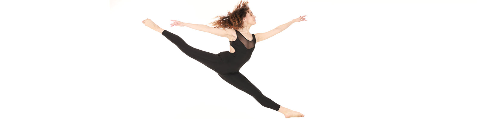 Dancer wearing a black dance unitard performing a graceful grand jeté against a white background for the dance unitard collection.