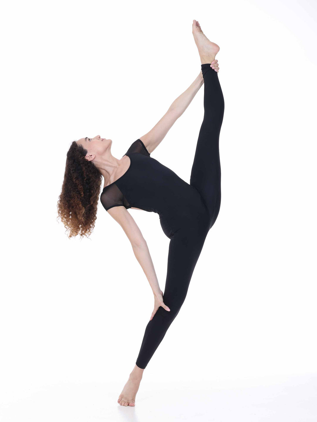 Danseuse portant la unitard de danse Sway – modèle Sheer Cap Sleeve Dance Unitard en negro, réalisant une extension de jambe haute en position de danza contemporánea, sur fond blanco.