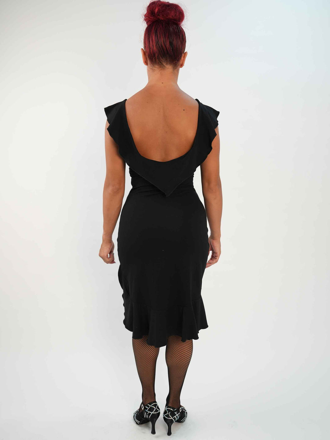 Mujer portant une vestido negroe de baile latino sin mangas, avec encolure volantée et ourlet asymétrique, associée à des medias résille et des zapatos de danza ornées. Tenue elegante et fluido, parfaite pour la salsa ou le ballroom. - vue de l&