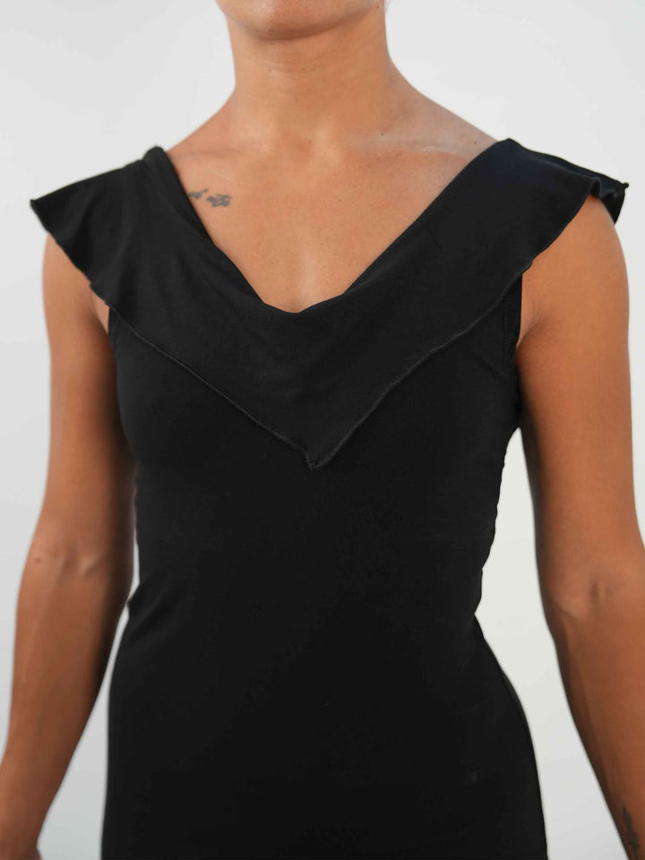 Mujer portant une vestido negroe de baile latino sin mangas, avec encolure volantée et ourlet asymétrique, associée à des medias résille et des zapatos de danza ornées. Tenue elegante et fluido, parfaite pour la salsa ou le ballroom. - gros plan de la vue de face